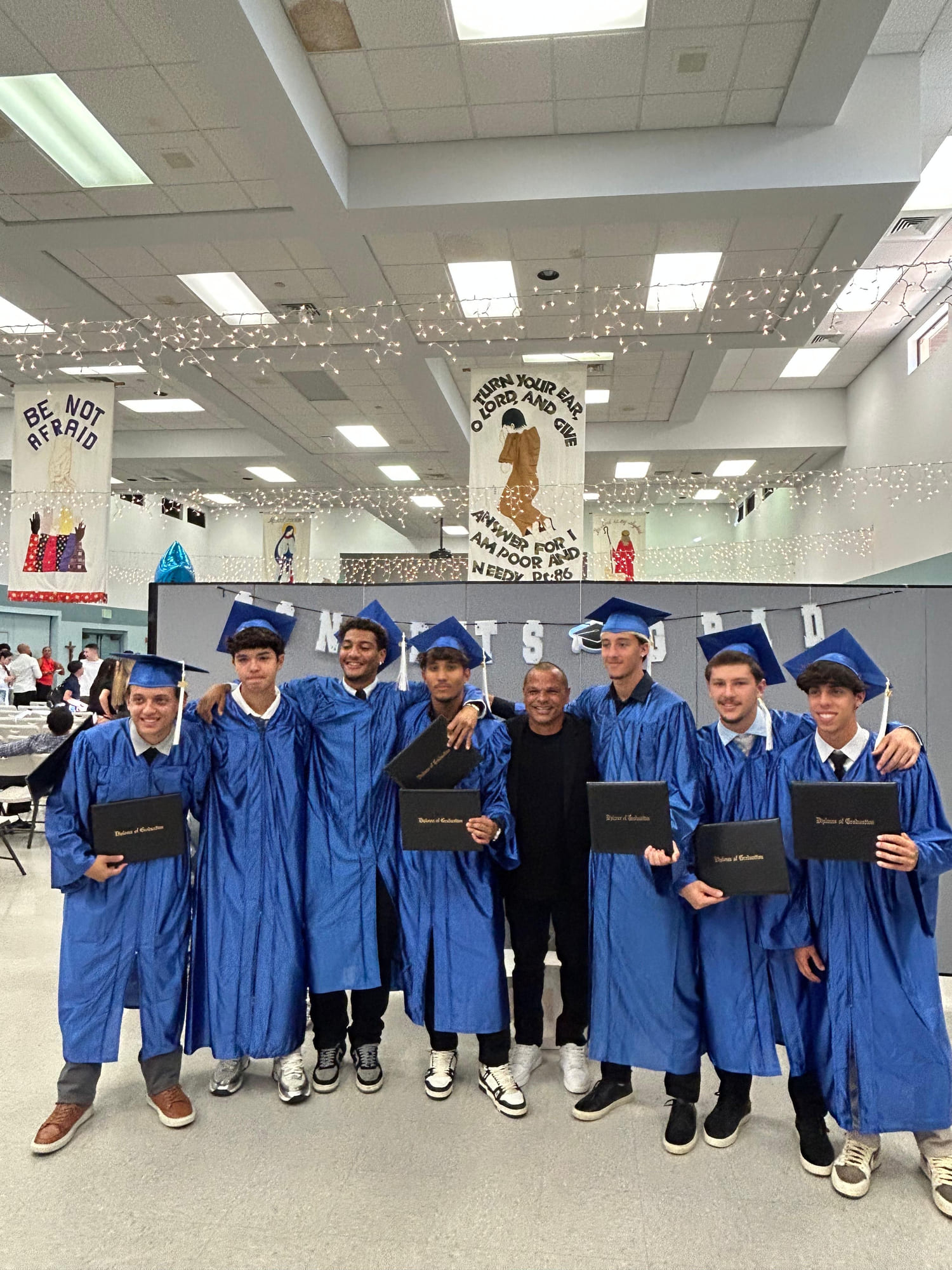 Arthur e colegas de turma na formatura, de beca azul e capelo, segurando os diplomas.